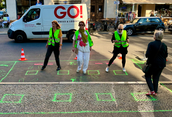 Bild von vier Frauen, die auf Gehweg und Straßenfläche tanzen.