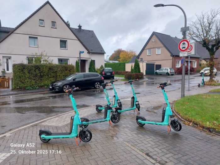 Das Foto zeigt einen Straßenbereich mit Gehwegen, die durch fünf platzierte E-Scooter blockiert werden