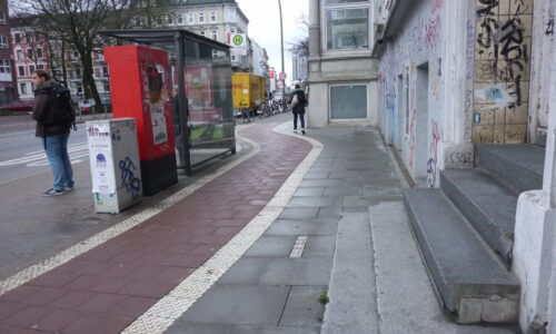 Ein neuer breiter Radweg mit beidseitiger Noppenmarkierung wird an Bushaltestelle vorbeigeführt. Der Gehweg ist zu schmal.