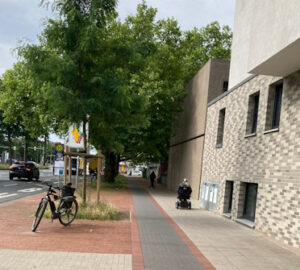 Foto: Ein Rollator und ein Rollstuhl auf einem 1,80 m breiten Gehweg. Der Bereich macht einen relativ frisch sanierten Eindruck. Die Begrenzung des schmalen Radweges zur Fahrbahn hin ist die Baumscheibe. Foto: Simons, FUSS e.V: