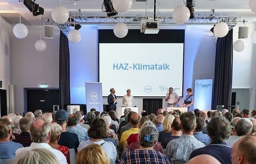 Ein Blick auf das Podium beim HAZ-Klimatalk. Im Vordergrund Zuschauhörerin.