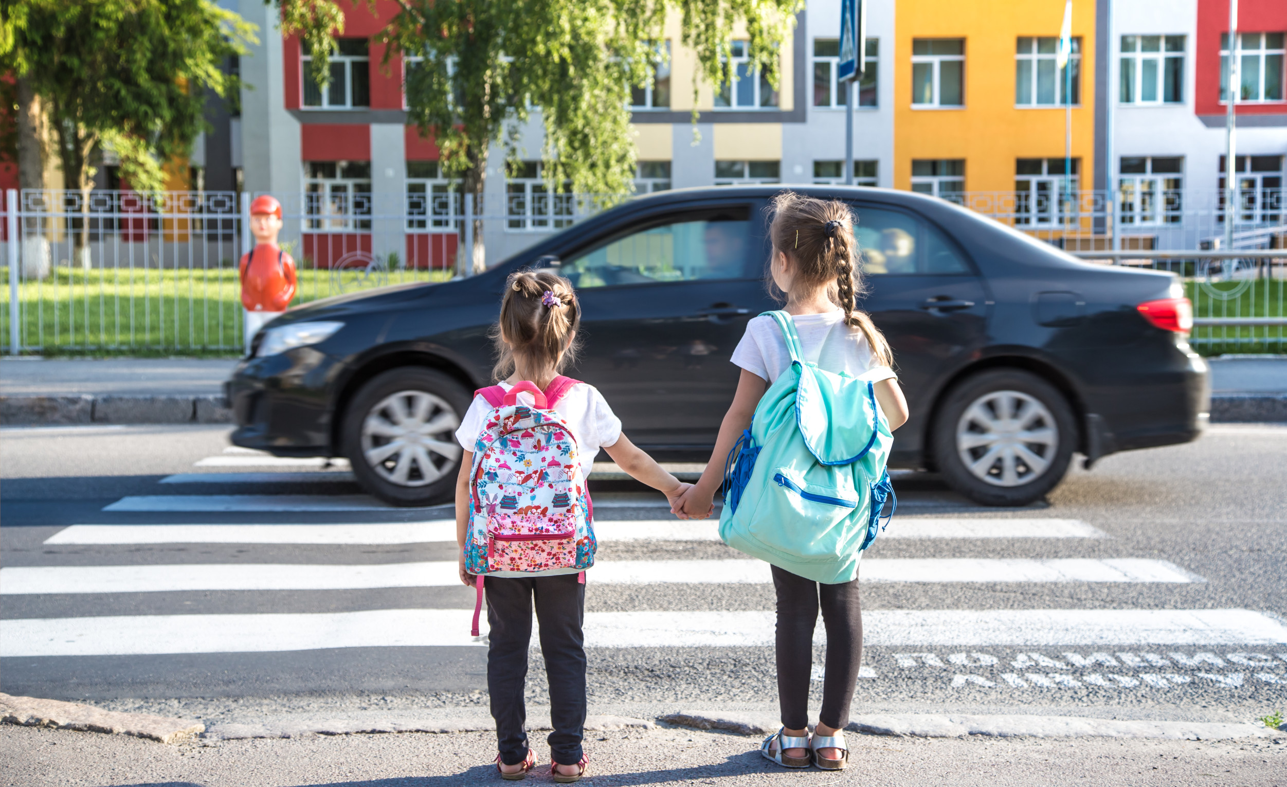 Zwei Kinder warten an einem Zebrastreifen, während ein Auto vorbeifährt