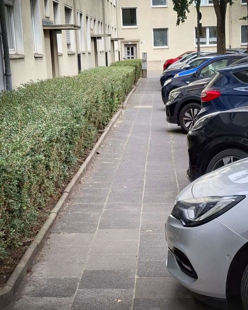 Autos sind schräg auf einem Gehweg geparkt und lassen nur wenig Platz für Zufußgehende