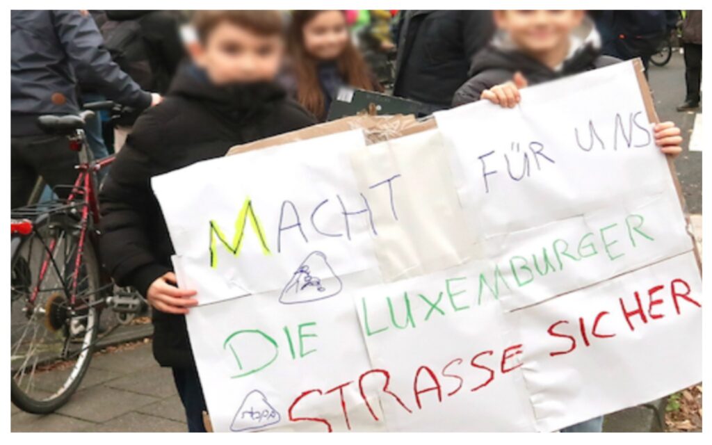 Kinder halten ein selbst gemaltes Plakat hoch mit dem Satz Macht für uns die Luxemburger Straße sicher; © Wolfgang Scheible