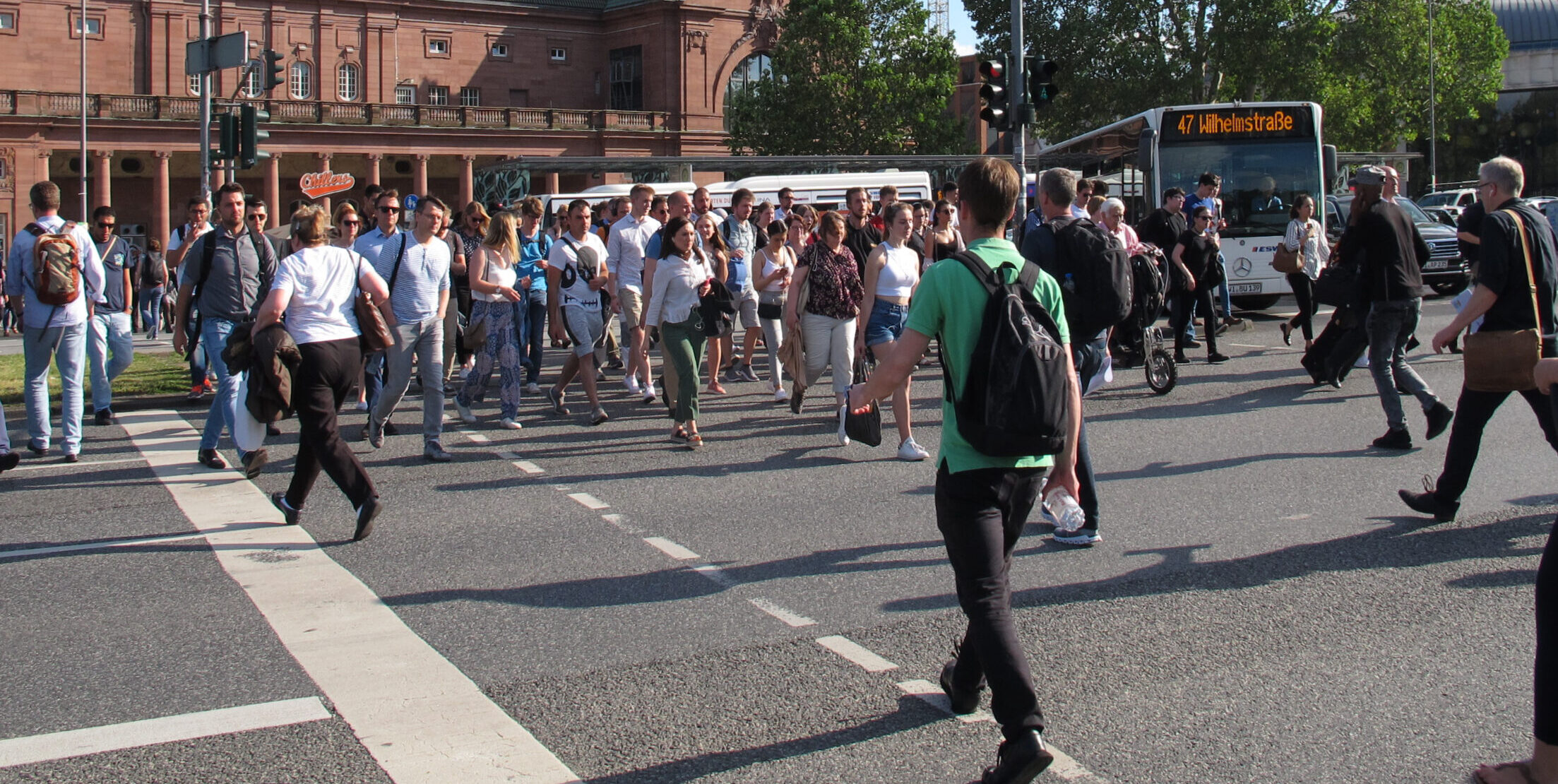 Viele Menschen überqueren eine Fußgängerampel vor dem Hauptbahnhof in Wiesbaden.