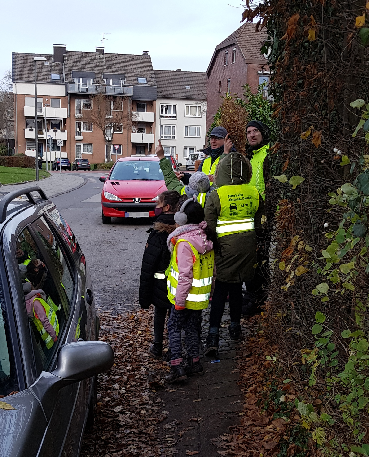 Gruppe mit Kindern quetscht sich an parkenden Autos vorbei