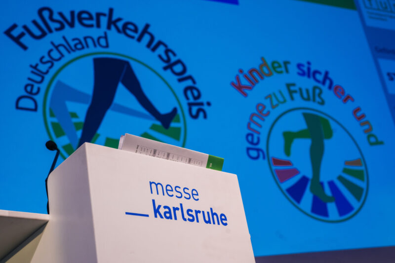 Logos des Fußverkehrspreis Deutschland auf der Leinwand, davor das Rednerpult mit der Aufschrift Messe Karlsruhe