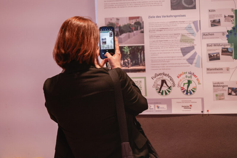 eine Teilnehmerin fotografiert die Postergalerie in der die hervorgehobenen Projekte des 2. Fußverkehrspreises Deutschland ausgestellt sind