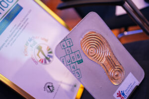 Urkunde und Trophäe des Sonderpreises: Goldener Schuhabdruck mit dem FUSS e.V.-Logo als Kinder-Hüpfspiel.
