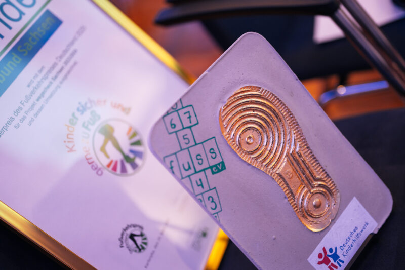 Urkunde und Trophäe des Sonderpreises: Goldener Schuhabdruck mit dem FUSS e.V.-Logo als Kinder-Hüpfspiel.