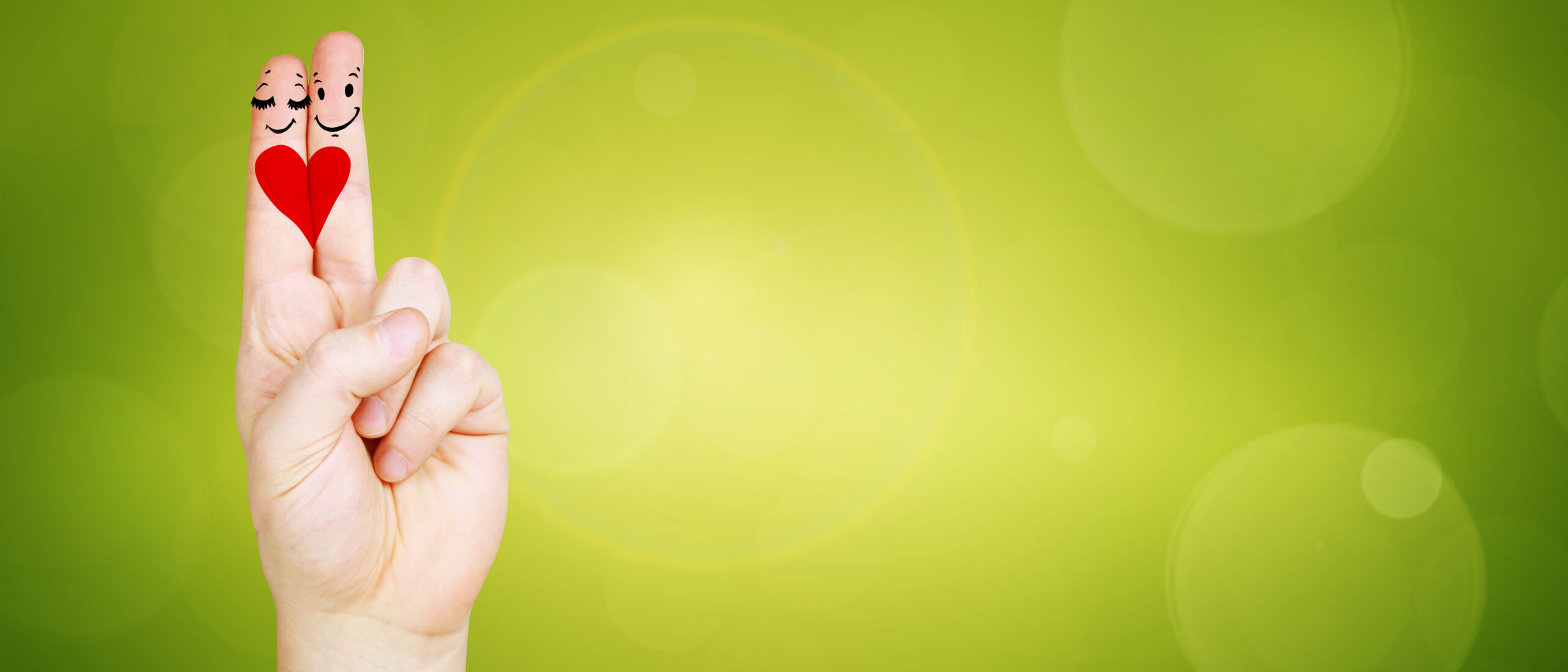 Mit Smileys und Herz bemalte Finger vor grünem Hintergrund