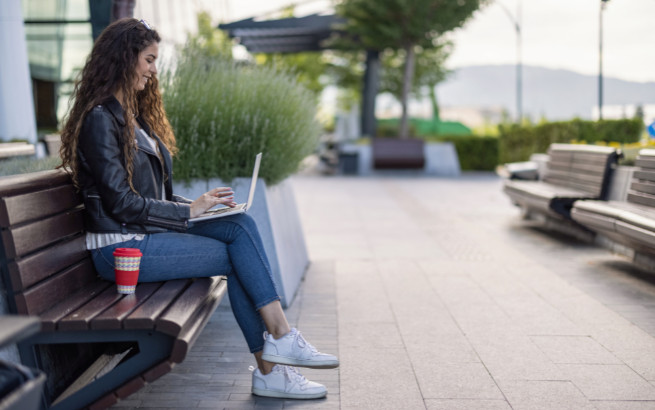 Frau mit Laptop auf einer Bank in einer Fußgängerzone