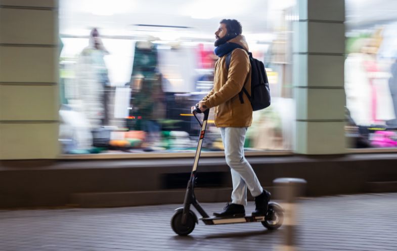 Mann fährt mit E-Scooter auf dem Gehweg