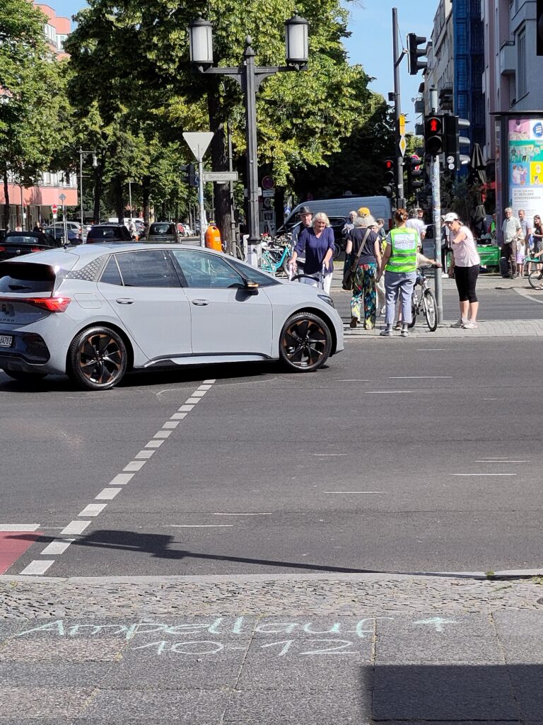 Auto biegt ab, Zufußgehnde warten auf Mittelinsel