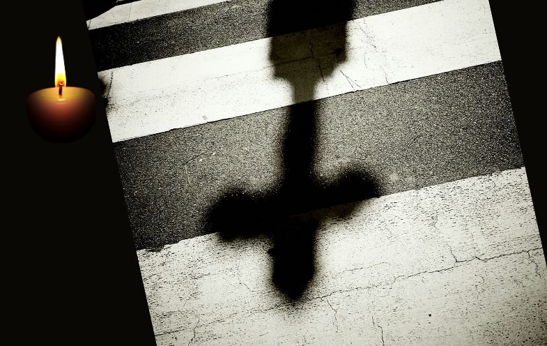 Ein Zebrastreifen mit Schatten einer Laterne, die wie ein Grabkreuz erscheint. Daneben eine Trauerkerze.