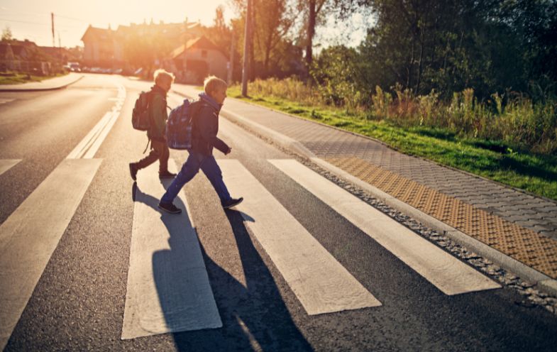 zwei Schulkinder überqueren einen Zebrastreifen über eine Schnellstraße