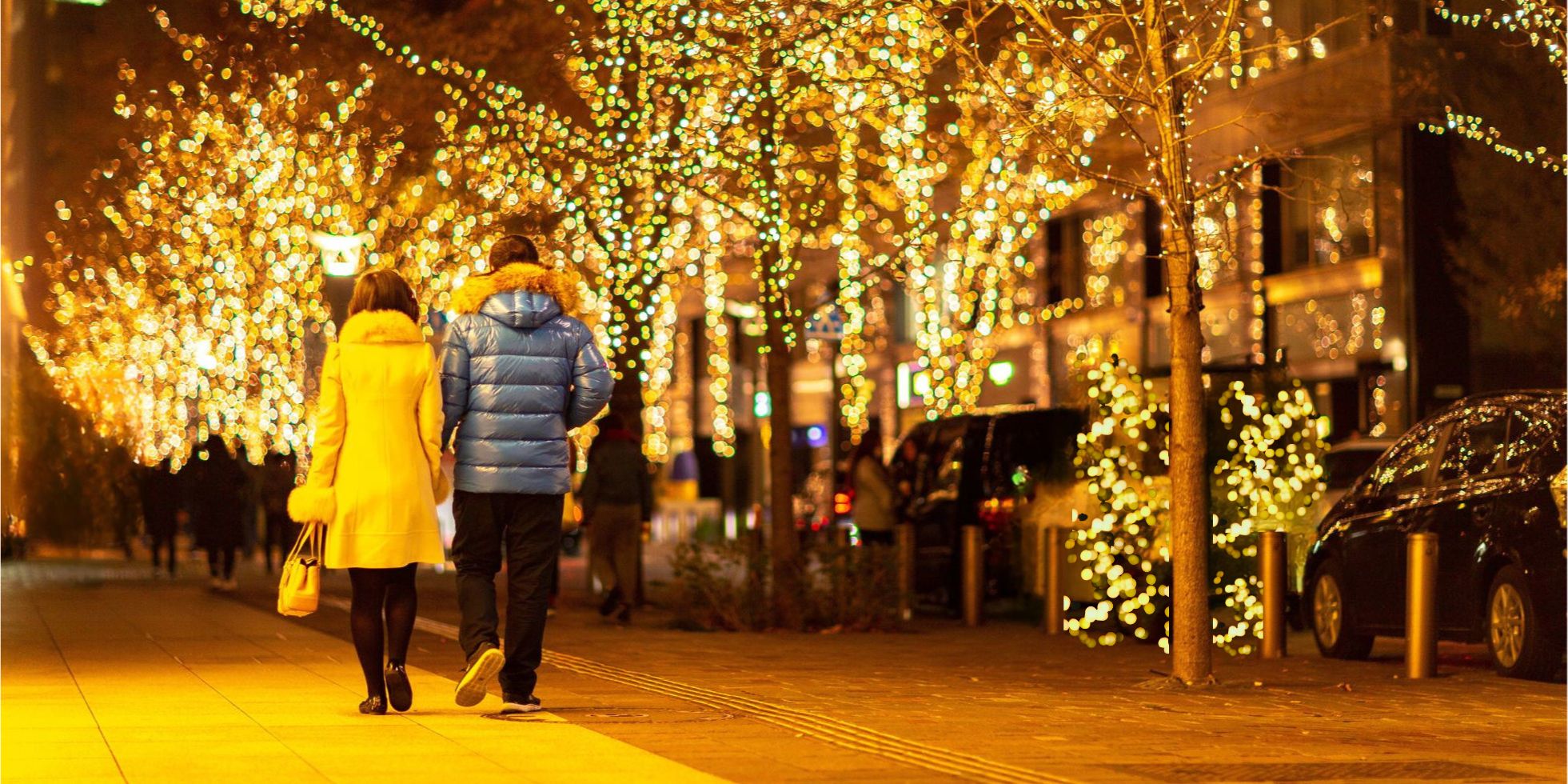 ein Paar geht zu Fuß über einen weihnachtlich beleuchteten Gehweg