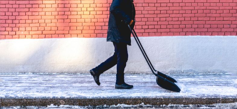 Mann schiebt Schnee auf einem Gehweg