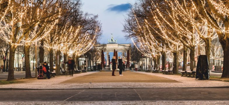 weihnachtlich beleuchteter Boulevard "Unter den Linden" in Berin. Im Vordergrund Fußgänger im Hintergrund das Brandenburger Tor