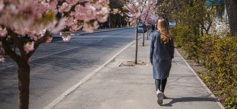Frau geht auf einem Gehweg, neben ihr blühende Obstbäume